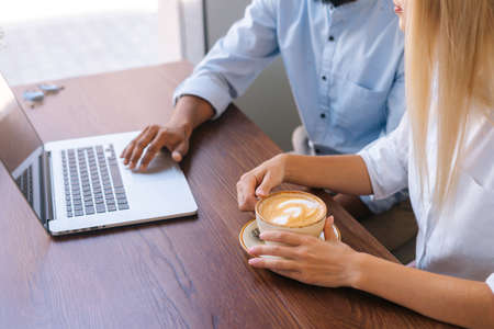 Close-up top view hands of unrecognizable business man and woman working with laptop sitting at table in cafe, finger on touchpad. Closeup view of female holding cup with hot coffee.の写真素材