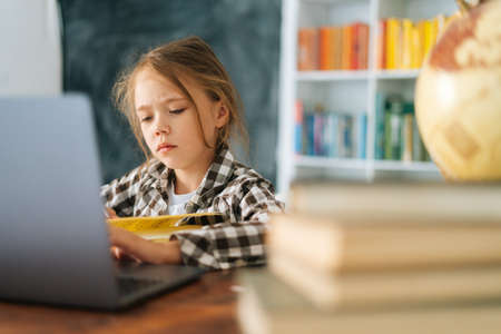 Close-up of serious unhappy cute elementary child school girl doing writing homework holding pen...