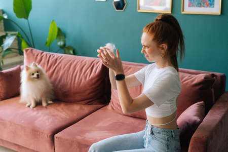 Displeased young woman with look of disgust on face looking on tuft of pet hair holding in hand....