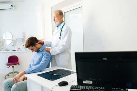 Professional mature adult male manual therapist turning and bending head of male patient to check his injured neck. Young man on preventive examination of doctor chiropractor on neck diagnostic.の写真素材