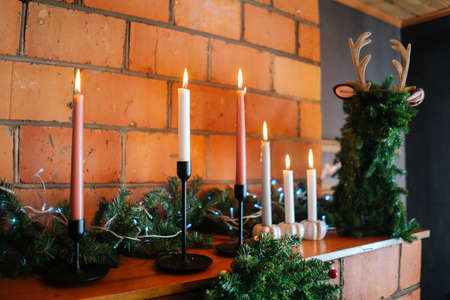 Close-up side view of beautiful deer ornament and Christmas wreath on brick fireplace with burning candles at cozy house. Preparing for xmas, new year and winter holidays, festive mood.の写真素材