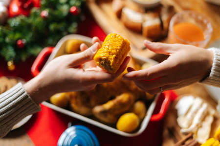 Close-up top view of unrecognizable young woman and man passing delicious boiled corn sitting at...