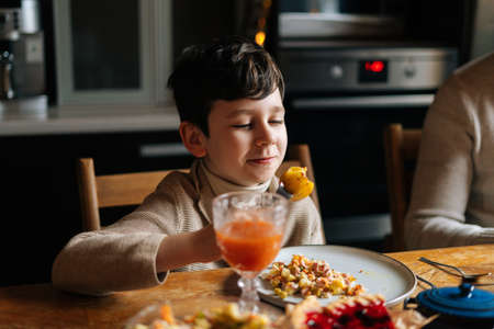 Medium shot of adorable child kid boy eating fried potatoes sitting at dinner feast table during holiday family party, selective focus, blurred background. Family having dinner Christmas party.の写真素材