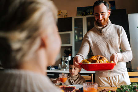 Close-up view from back of unrecognizable woman to young man putting dish with grilled hot turkey on...
