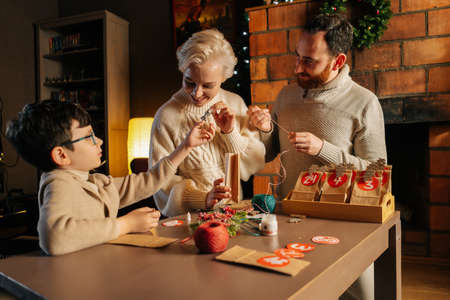 Joyful young family making Christmas advent calendar together sitting at table on background of fireplace in cozy house on xmas Eve, enjoying togetherness preparing for holidays at home.の写真素材