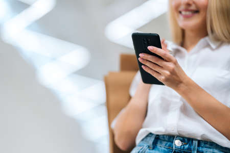 Close-up cropped shot of unrecognizable cheerful blonde young woman using mobile phone, holding...