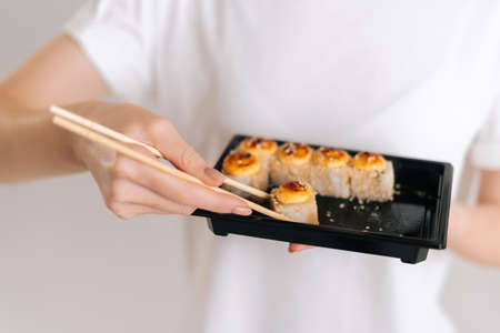 Close-up hands of unrecognizable young woman taking fresh sushi rolls with chopsticks on white isolated background in studio. Pretty Caucasian female eating Asian food.の写真素材