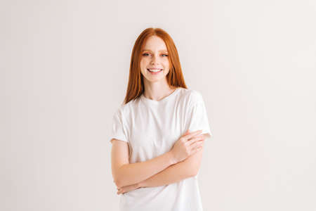 Portrait of smiling pretty young woman looking at camera standing with crossed arms on white...