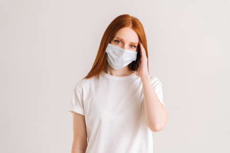 Studio portrait of attractive young woman wearing casual t-shirt and protective face mask looking at camera standing on white isolated background. Flu epidemic, dust allergy, protection against virus.の写真素材