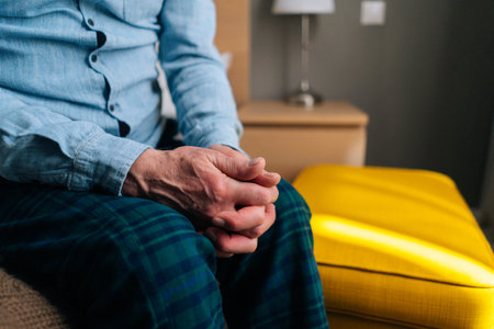 Close-up cropped shot of unrecognizable senior adult nervous male rubbing hands in trouble and demonstrating stress, anger, irritation, sitting in sofa at home alone.の写真素材