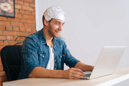 Side view of crazy smiling male conspiracy theorist wearing aluminum foil protect brain watching...