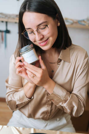 Vertical close-up view of happy young woman in glasses holding little transparent glass jar with...