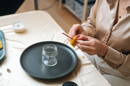 Close-up high-angle view of unrecognizable female artisan using piece of beeswax to create wick for handmade candle at workshop. Process of making hand-made natural candle at home.の写真素材