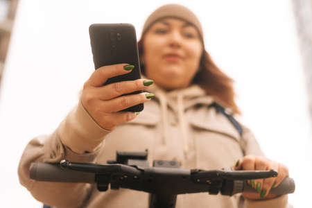 Close-up low-angle view of woman wearing warm hat and outerwear using mobile phone standing with...
