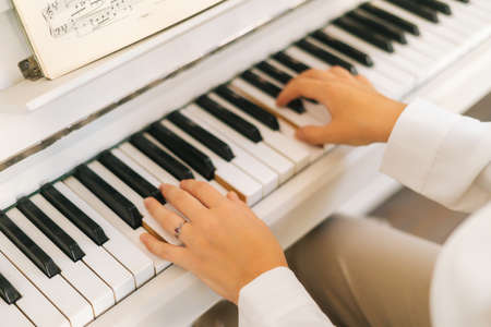 Close-up high-angle view of unrecognizable female musician performer playing on classical piano at...