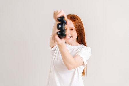 Studio portrait of joyful pretty young woman playing video game with controller looking at camera on...