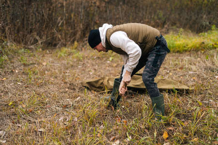 Focused tourist male wearing warm clothes digging fire place using small shovel at outdoors on...