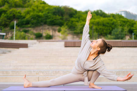 Front view of flexible young yogini woman practicing yoga exercisers on fitness mat on summer day...