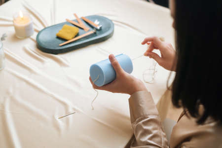 Close-up back view of unrecognizable female artisan putting wick through silicone mold preparing for pouring liquid wax. Process of making handmade natural candle at workshop.の写真素材