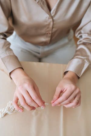 Close-up vertical shot of unrecognizable woman putting thread through eye of needle sitting at...