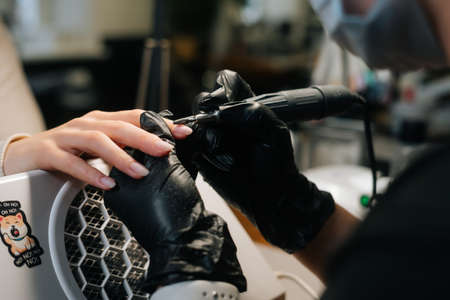 Close-up cropped shot of unrecognizable female manicurist removing gel polish or acrylic from nails with help of manicure machine. Concept beauty industry customer serviceの写真素材