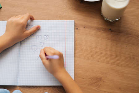 Close-up cropped shot of unrecognizable elementary little child girl drawing with pen doing homework...