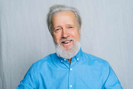 Close-up portrait of cheerful gray-haired senior man looking at camera on white isolated background....