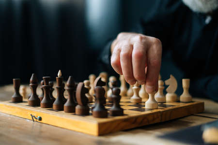 Close-up hands of unrecognizable bearded chess player performing move with pawn piece on wooden chessboard, selective focus. Closeup of board chess game execution of move by player grandmasterの写真素材