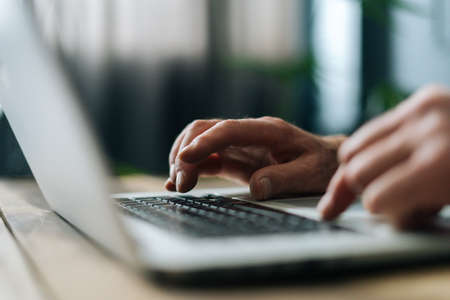 Close-up side view of unrecognizable mature adult man writing text on portable wireless computer...