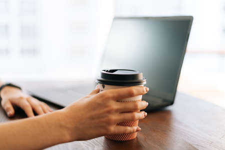 Close-up hands of unrecognizable young business woman sitting at desk with laptop in modern office...