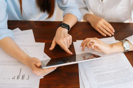 Close-up high-angle view of hands unrecognizable two young business women using digital tablet at...