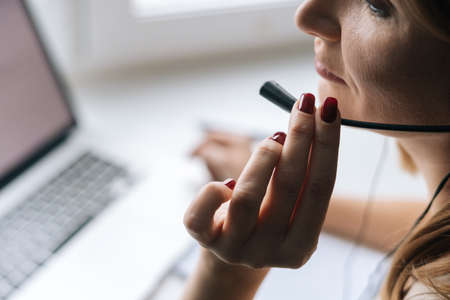 Close-up cropped shot of female operator talking using headset and consulting client sitting at...