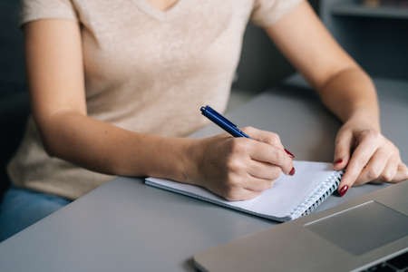 Close-up cropped shot of unrecognizable woman write making notes, studying online on laptop at home...