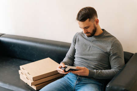 Courier male holding using payment POS wireless terminal waiting customer, sitting on sofa with...