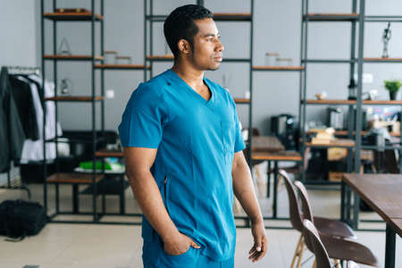Portrait of confident African American man doctor wearing medical lab uniform standing in hospital office, looking away. Front view of experienced nurse male posing at workplace.の写真素材