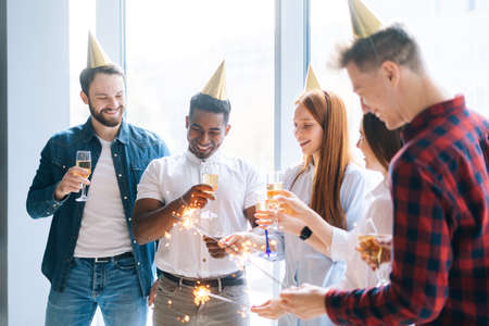 Cheerful business team of young multiethnic start-up businesspeople holding Bengal lights and...