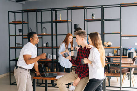 Group of five happy young business multiethnic start-up colleagues enjoying pleasant conversation...