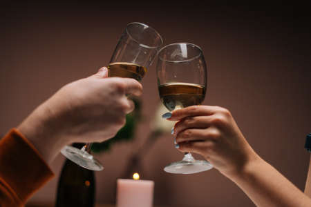 Close-up unrecognizable of happy young couple clinking glasses with wine at table with candles in...