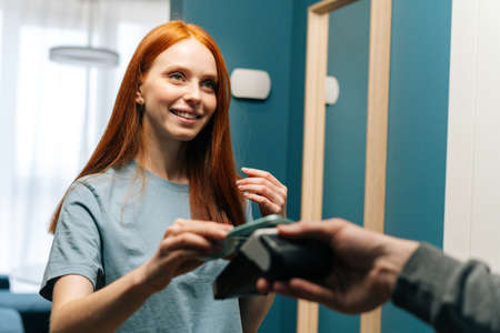 Close-up of smiling young woman customer making contactless payment using smartphone using POS wireless terminal to delivery man, on entryway at apartment, cropped shot.の写真素材