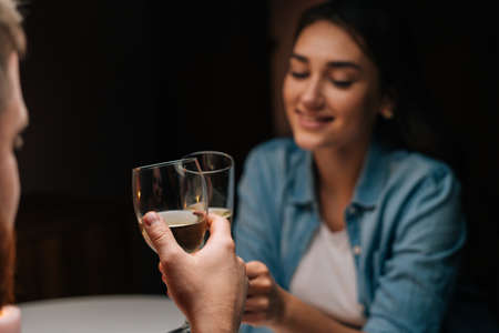 Close-up of happy young couple clinking glasses with wine sitting at table with candles in cozy dark room. Loving man and woman celebrating anniversary, Valentines day, enjoying romantic date.の写真素材