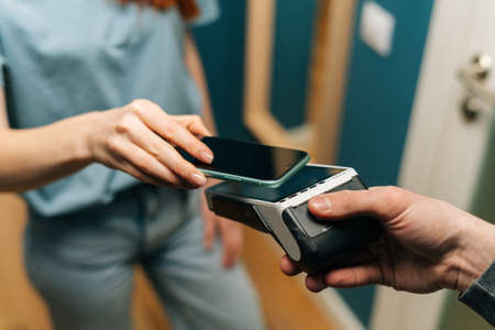 Close-up high-angle view of unrecognizable courier male giving POS wireless terminal to making...