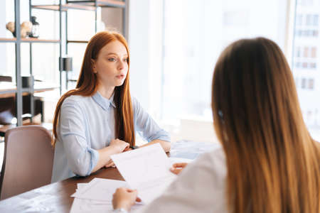 Close-up back view of two young businesswomen discussing new project sharing ideas sitting at desk...