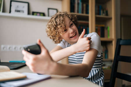 Laughing cute little girl holding and using mobile phone showing thumb up, browsing social network...