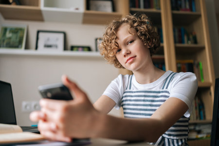 Close-up low-angle view of little schoolgirl pupil student e-learning, using smartphone for remote education, checking homework, preparing for test lessons sitting at desk with laptop and books.の写真素材