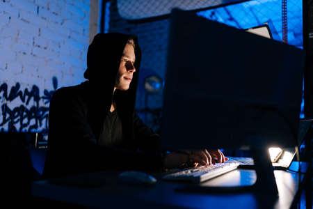 Low-angle view of wanted hacker coding virus ransomware using laptops and computers sitting at table...