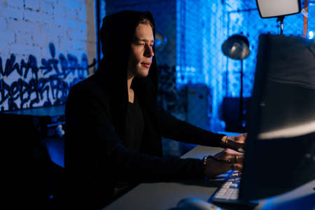 Side view of male hacker wearing hoods hacking to steal important information using computer to...