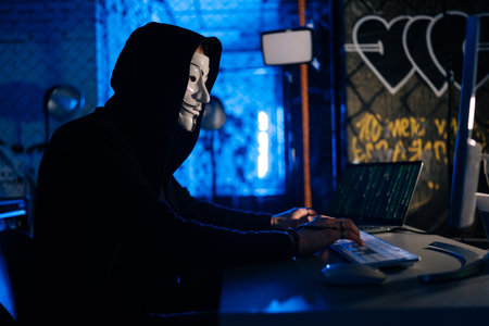 Dangerous hacker male wearing anonymous mask breaking computer system and typing password for...