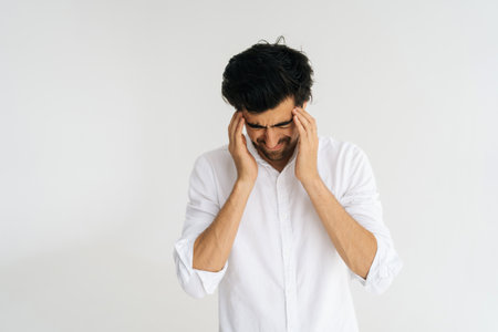 Studio portrait of depressed young man with closed eyes massaging temples suffering from headache painful, migraine, doubt make complicated decision standing on white isolated background.の写真素材