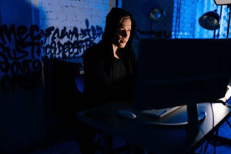Medium shot portrait of hidden hacker man wearing sweatshirt with hood engaged in hacking into...