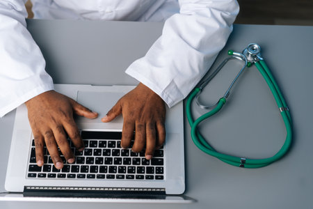 Close-up top view of unrecognizable African practitioner male doctor in white coat uniform working...